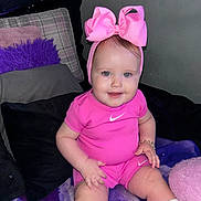 Frankie-Rae joined the competition — help win amazing prizes! baby, child, pink_clothing, headband, bow, smiling, sitting, couch, pillow, bracelet, white_socks, indoor, cute, portrait, young_child, person, happy, fashion, infant, apparel