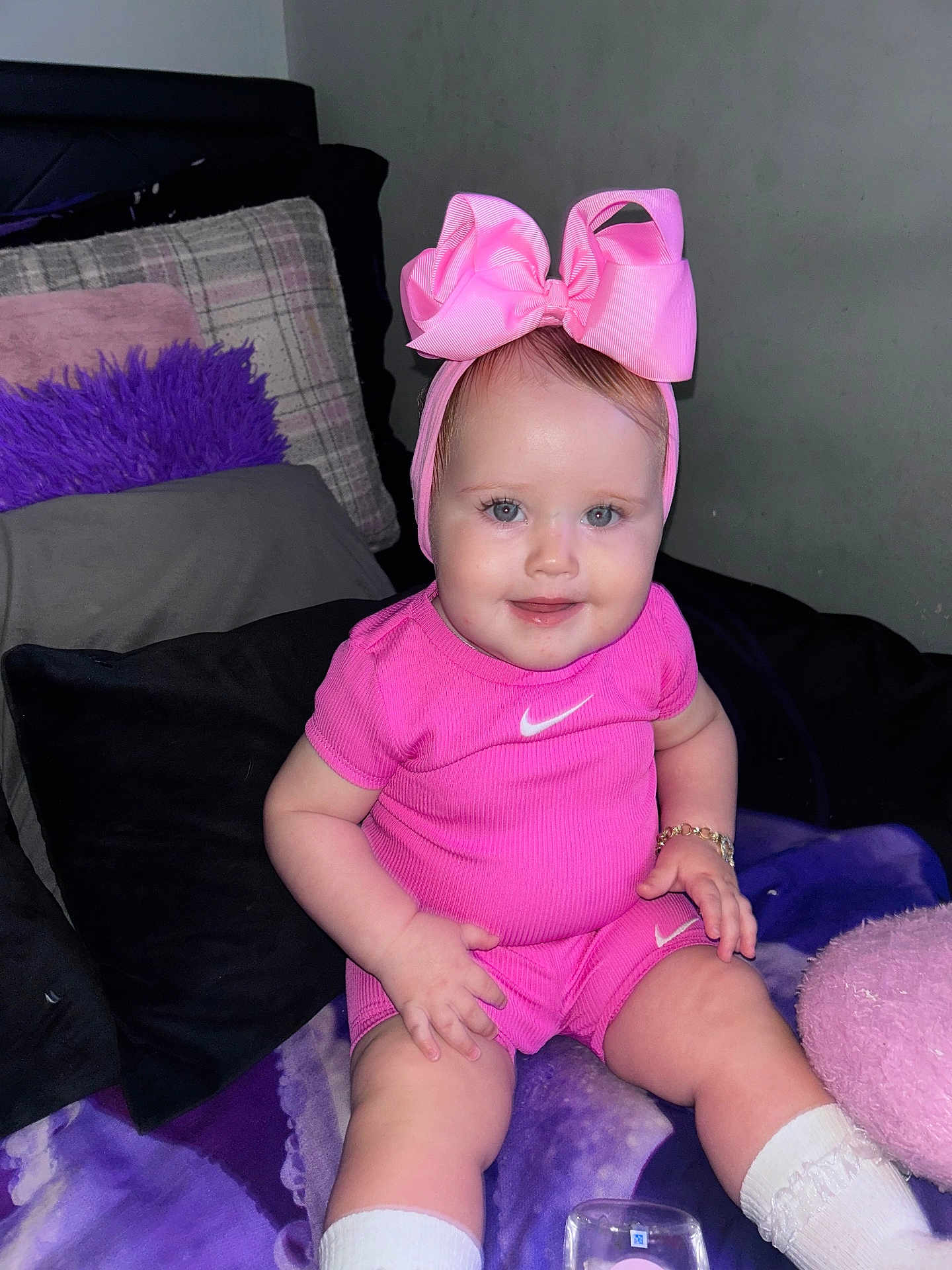 Frankie-Rae joined the competition — help win amazing prizes! baby, child, pink_clothing, headband, bow, smiling, sitting, couch, pillow, bracelet, white_socks, indoor, cute, portrait, young_child, person, happy, fashion, infant, apparel