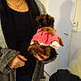 Rozenn a rejoint le concours — aidez-le/la à gagner de superbes lots ! black_shirt, brown_fur, coat, cute, dog, door, furniture, gray_cardigan, hand, holding, indoor, jewelry, living_room, necklace, person, pet, pink_clothing, puppy, small_dog, wall