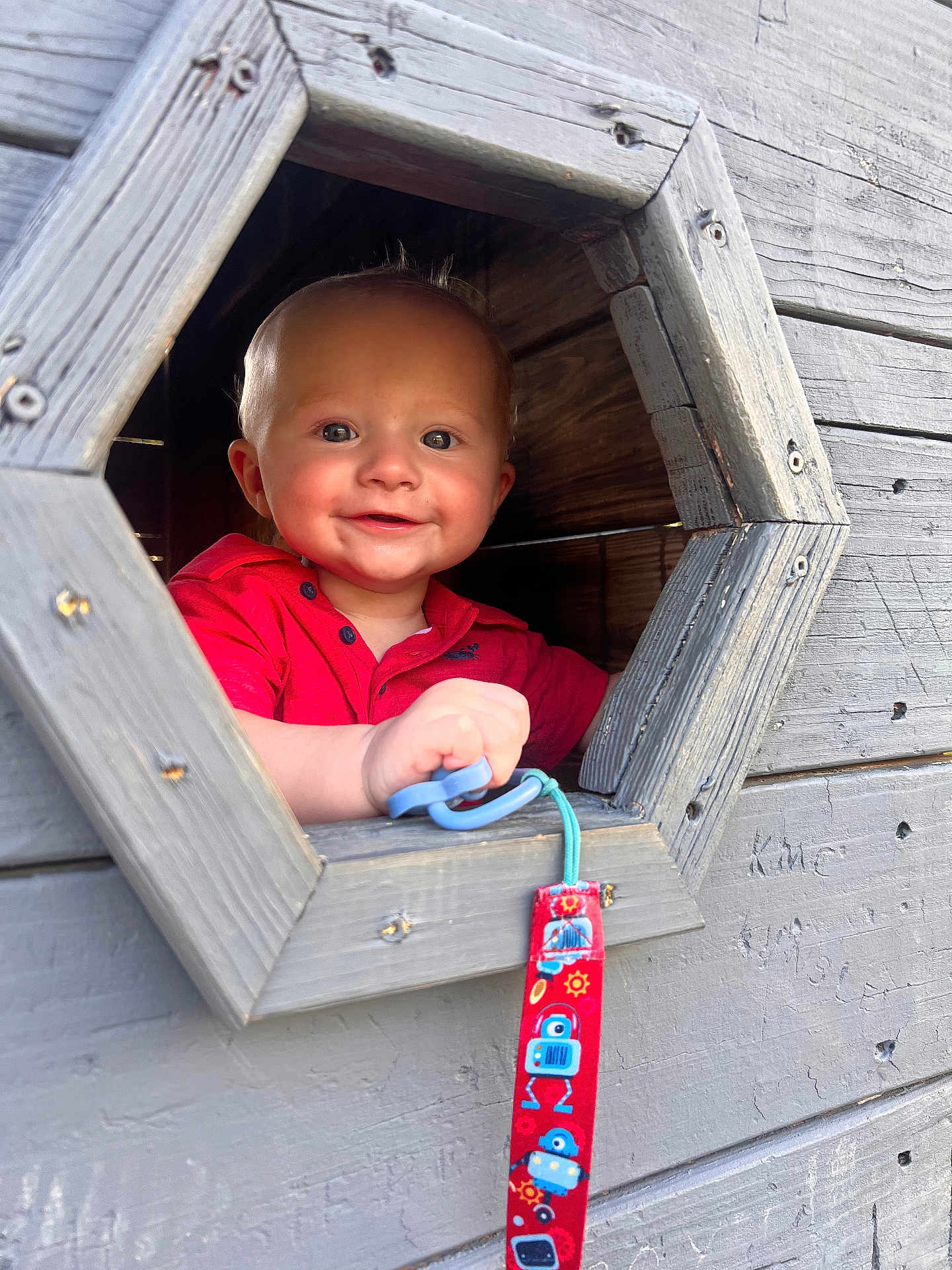 Maverick is registered to the contest to win money with this photo: toddler, child, smiling, red_shirt, pacifier, wooden_structure, window, face, hand, toy, playhouse, outdoor, cute, happy, infant, portrait, baby, colorful, blue, grip