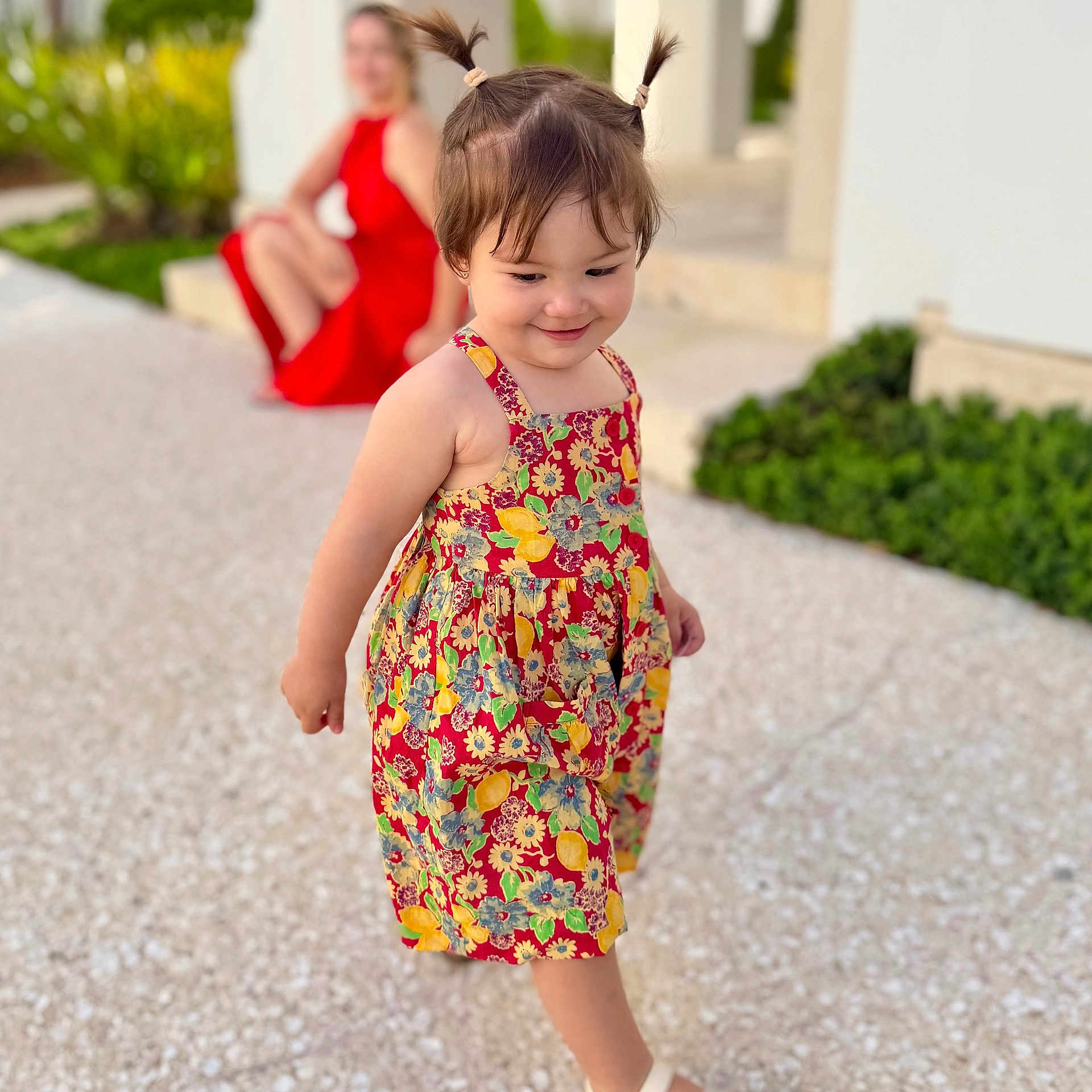 Emma joined the competition — help win amazing prizes! toddler, child, girl, flower_dress, pigtails, walking, outdoor, smiling, portrait, blurred_background, woman, red_dress, pavement, greenery, happy, summer, casual, daylight, playful, person