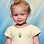 toddler, child, portrait, smiling, yellow_shirt, curly_hair, flower_embroidery, cute, face, blue_background, studio_photo, innocent, young_child, short_sleeves, light_skin, indoor, happy, baby, person, headshot