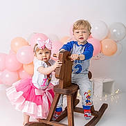 Aliyah is registered to the contest to win money with this photo: toddler, child, rocking_horse, balloons, pink_tutu, bow, blue_shirt, gray_pants, socks, playing, indoor, studio, cute, smiling, fun, toy, celebration, birthday, wooden_toy, happy