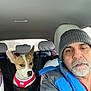 Krystal is registered to the contest to win money with this photo: adult, animal, beanie, car, car_seat, casual_clothing, dog, gray_hair, harness, indoors, jacket, looking_away, man, pet, portrait, rain, seat_cover, vehicle_interior, white_beard, window