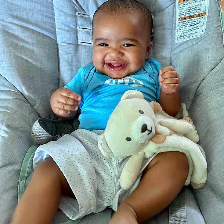 Jamari joined the competition — help win amazing prizes! baby, baby_seat, blue_shirt, child, clothing, comfort, cute, foot, furniture, hand, happy, indoor, infant, person, plush_toy, seatbelt, shorts, skin, smiling, teddy_bear