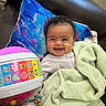 Athena joined the competition — help win amazing prizes! baby, smiling, blanket, toy, alphabet, ball, couch, pillow, child, indoor, happy, curly_hair, clothing, person, playful, colorful, soft_texture, infant, seated, cozy