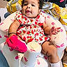 baby, blanket, bunny_pattern, child, colorful, cup, curly_hair, cute, dress, earrings, indoor, infant, inflatable_seat, person, pillow, pink_socks, portrait, smiling, strawberry_pattern, watermelon_pattern