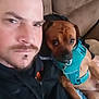 man, dog, couch, indoor, closeup, pet, harness, casual_clothing, beard, mustache, brown_dog, human_face, animal_face, seated, relaxed, furniture, expression, bond, friendship, companion