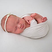 Ivy is registered to the contest to win money with this photo: newborn, baby, sleeping, wrapped, white_blanket, headband, flower, infant, peaceful, soft_light, portrait, cute, tiny_feet, close_up, skin, resting, serene, wrapped_in_blanket, lying_down, studio_photo