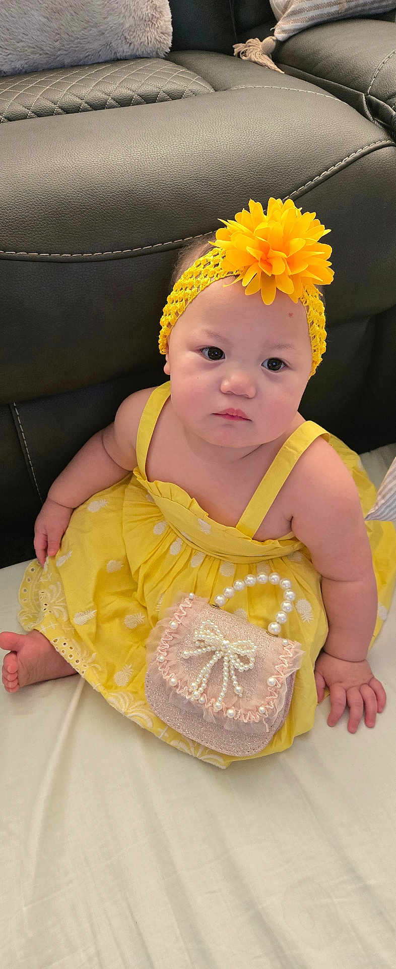 Melody Reign joined the competition — help win amazing prizes! baby, child, yellow_dress, headband, flower, purse, pearl, sitting, indoor, couch, black_leather, cushion, cute, infant, portrait, person, soft_toys, decor, bed, skin