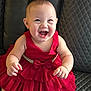 baby, child, red_dress, smiling, happy, leather_couch, seated, infant, cute, portrait, indoors, joyful, dress, clothing, person, skin, face, hands, foot, fashion