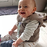 Mylan participe au concours pour gagner de l'argent avec cette photo : baby, child, clothing, cute, dog_pattern, floor, happy, home, indoor, light, pacifier, pants, plant_pot, rug, shirt, shoes, sitting, smiling, toddler, vest