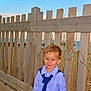 child, boy, smile, striped_shirt, tie, wooden_fence, beach, ocean, sky, grass, sand, outdoor, portrait, casual_clothing, sunlight, young_child, nature, happy, standing, blond_hair