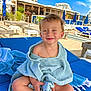 toddler, child, smile, striped_towel, beach, lounge_chair, sunny, blue_sky, umbrella, sand, resort, outdoor, happy, portrait, vacation, relaxation, clothing, person, summer, holiday