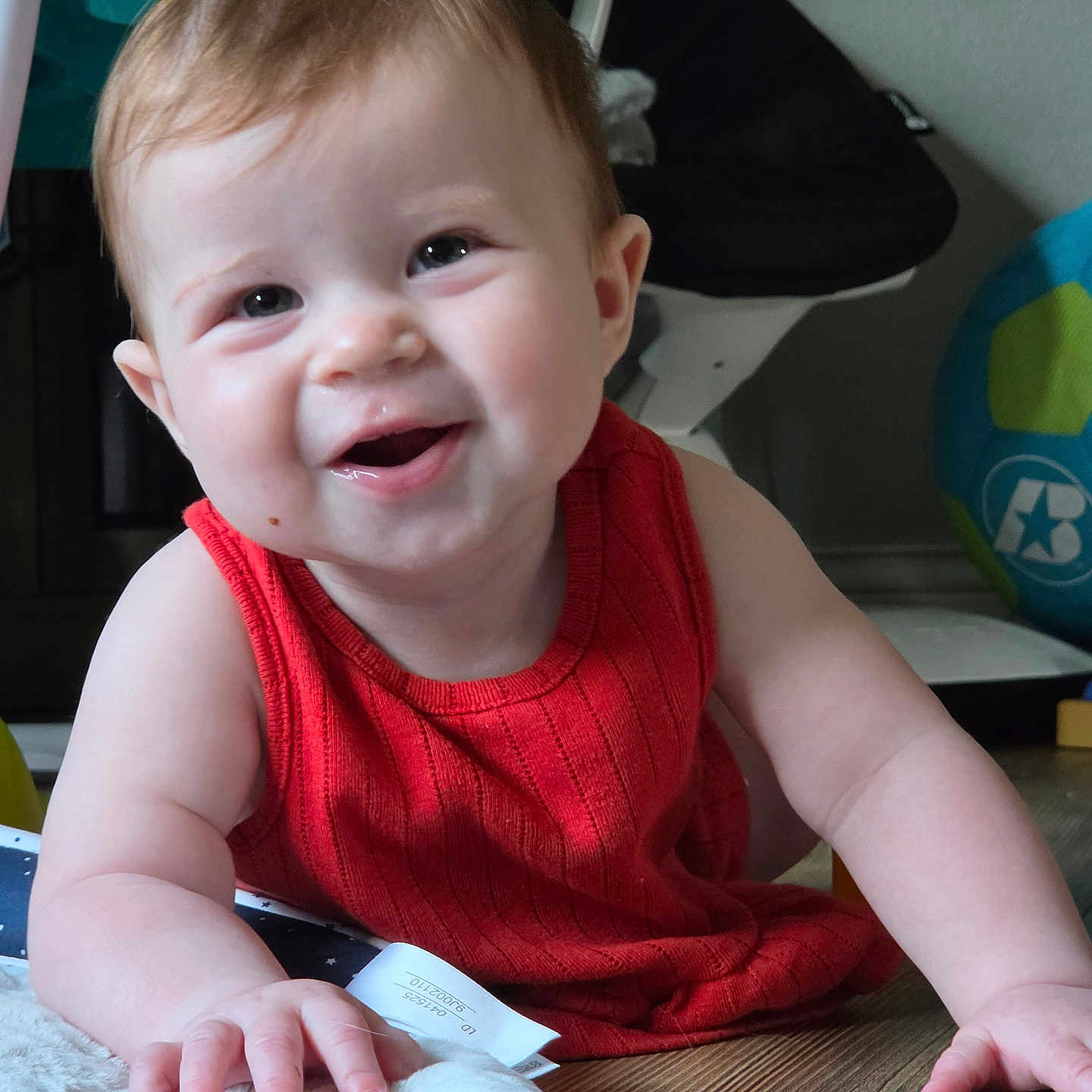 Zoey is registered to the contest to win money with this photo: baby, child, crawling, red_clothing, smiling, happy, indoor, wooden_floor, face, arms, hand, furniture, toy, home, cute, infant, skin, person, portrait, young_child