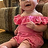 baby, infant, smiling, pink_clothing, sitting, carpet, couch, indoor, child, cute, happy, person, young_child, furniture, hand, portrait, ruffles, skin, legs, expression