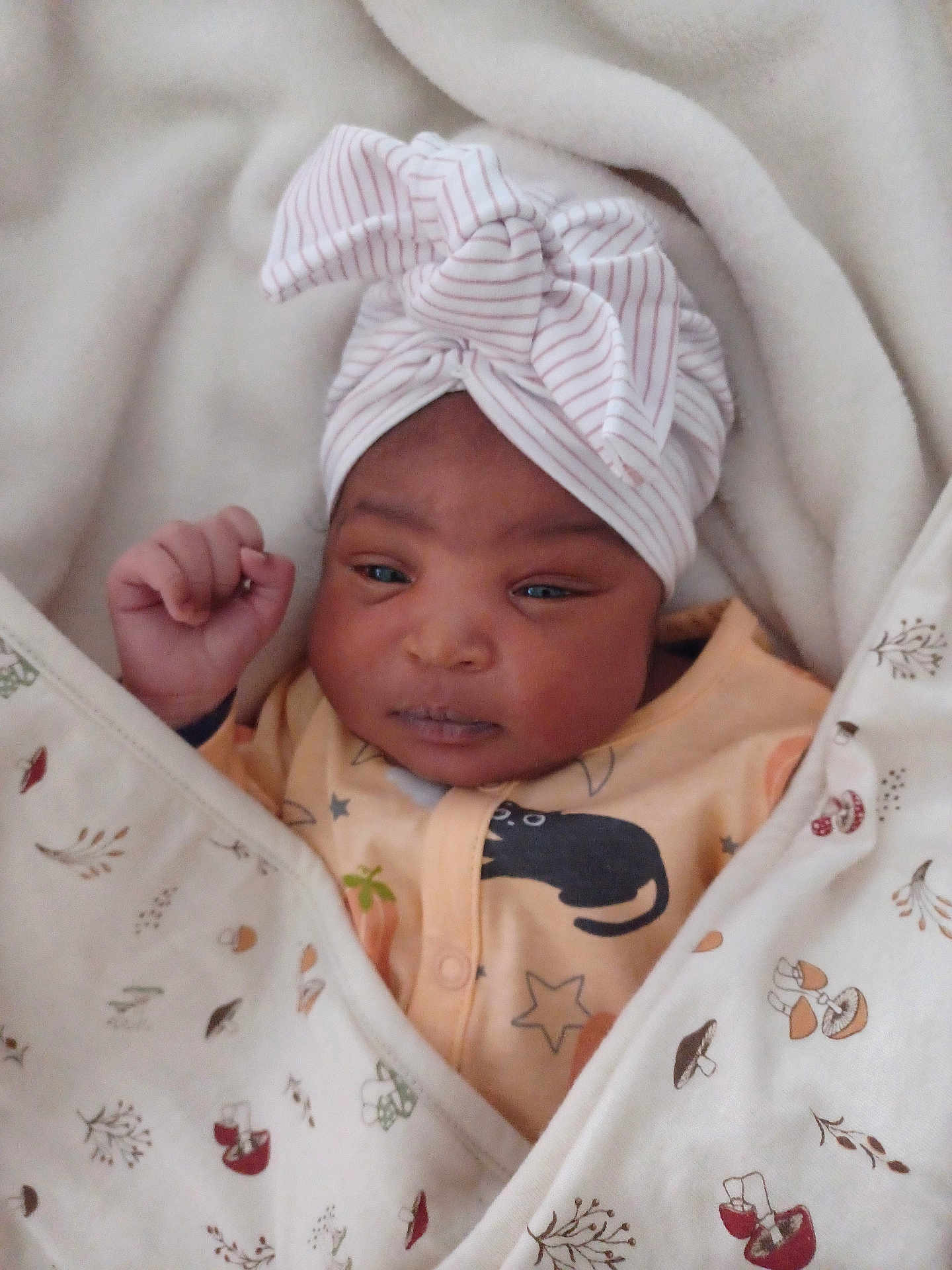 ëziah-Kimoya a rejoint le concours — aidez-le/la à gagner de superbes lots ! baby, blanket, head_wrap, infant, clothing, face, person, sleepwear, pattern, newborn, cute, wrapped, soft, fist, expression, indoor, closeup, warm, resting, adorable