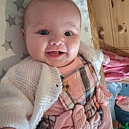 Emma-Leigh joined the competition — help win amazing prizes! baby, smiling, child, infant, knitted_cardigan, pink_dress, plaid_pattern, bows, happy, face, lying_down, stars_pattern, wooden_furniture, indoor, cute, person, apparel, toy, room, candid
