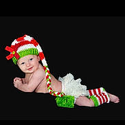 Clara is registered to the contest to win money with this photo: baby, infant, smiling, hat, knitted, red, white, green, bow, leg_warmers, diaper_cover, frilly, cute, lying_down, portrait, blue_eyes, holiday, festive, black_background, child