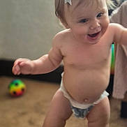 Charlotte is registered to the contest to win money with this photo: baby, child, diaper, bow, walking, carpet, indoor, smiling, happy, person, toddler, skin, face, head, limbs, blurred_background, toy, colorful, candid, cute