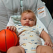 Theo is registered to the contest to win money with this photo: baby, infant, basketball, baby_seat, clothing, onesie, toy, hand, face, chubby, indoor, plush, cushion, child, person, cute, expression, furniture, comfort, relax