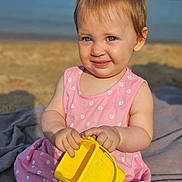 Emilia a rejoint le concours — aidez-le/la à gagner de superbes lots ! beach, blanket, blue_eyes, bucket, child, cute, daytime, hair, happy, outdoor, pink_dress, play, sand, sitting, skin, smile, summer, sunlight, toddler, toy