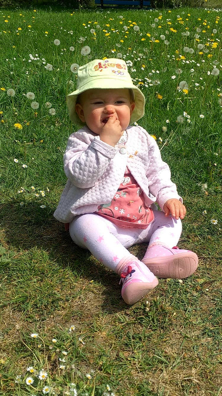 Mylena participe au concours pour gagner de l'argent avec cette photo : baby, baby_toddler_clothing, botany, cap, costume_hat, face, flower, grass, grass_family, happy, hat, headwear, leaf, meadow, people_in_nature, person, petal, pink, plant, smile