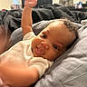 Elaysha is registered to the contest to win money with this photo: arms_up, baby, blanket, child, closeup, cozy, curly_hair, cute, expression, face, happy, home, indoor, infant, lying_down, person, pillow, playful, smile, soft_lighting