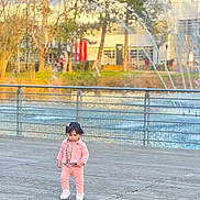 Aylin participe au concours pour gagner de l'argent avec cette photo : child, toddler, pink_clothing, walking, boardwalk, water_fountain, outdoor, daylight, trees, river, railing, building, person, footwear, casual_wear, nature, young_child, scenic, sunlight, park
