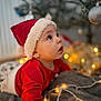 toddler, child, santa_hat, red_clothing, christmas_lights, blanket, holiday, indoor, decorations, tree, bokeh, face, portrait, cute, festive, warm_lighting, expression, cozy, curious, celebration