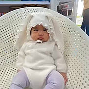 Isabel joined the competition — help win amazing prizes! baby, child, bunny_costume, white_clothing, purple_socks, ruffled_hood, plastic_chair, perforated_chair, indoor, store_shelves, snack_packages, containers, person, doorway, natural_light, seated, cute, portrait, curious, casual