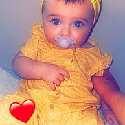 Nayna a rejoint le concours — aidez-le/la à gagner de superbes lots ! baby, infant, pacifier, headband, bow, yellow_outfit, blue_eyes, sitting, adult_arm, heart_sticker, onesie, portrait, cute, chubby_cheeks, blanket, indoor, closeup, hands, skin, looking_at_camera