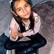 Sayna a rejoint le concours — aidez-le/la à gagner de superbes lots ! child, girl, peace_sign, headband, long_hair, brown_eyes, sitting, cross_legged, black_boots, leather_pants, pink_top, carpet, rug, indoor, flash_photography, smile, portrait, candid, person_in_background, electrical_cord