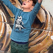 Emilio participe au concours pour gagner de l'argent avec cette photo : child, boy, happy, joyful, arms_raised, blue_long_sleeve, monster_shirt, green_pants, graffiti_wall, mural, street_art, leaves, autumn_leaves, outdoor, portrait, candid, expressive, face, hair, sidewalk