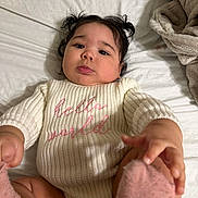 Sheraelys is registered to the contest to win money with this photo: baby, child, infant, pigtails, sweater, knitwear, bed, blanket, pink_socks, hand, face, cute, indoors, soft_texture, curious, lying_down, cozy, portrait, young_child, warm_clothing