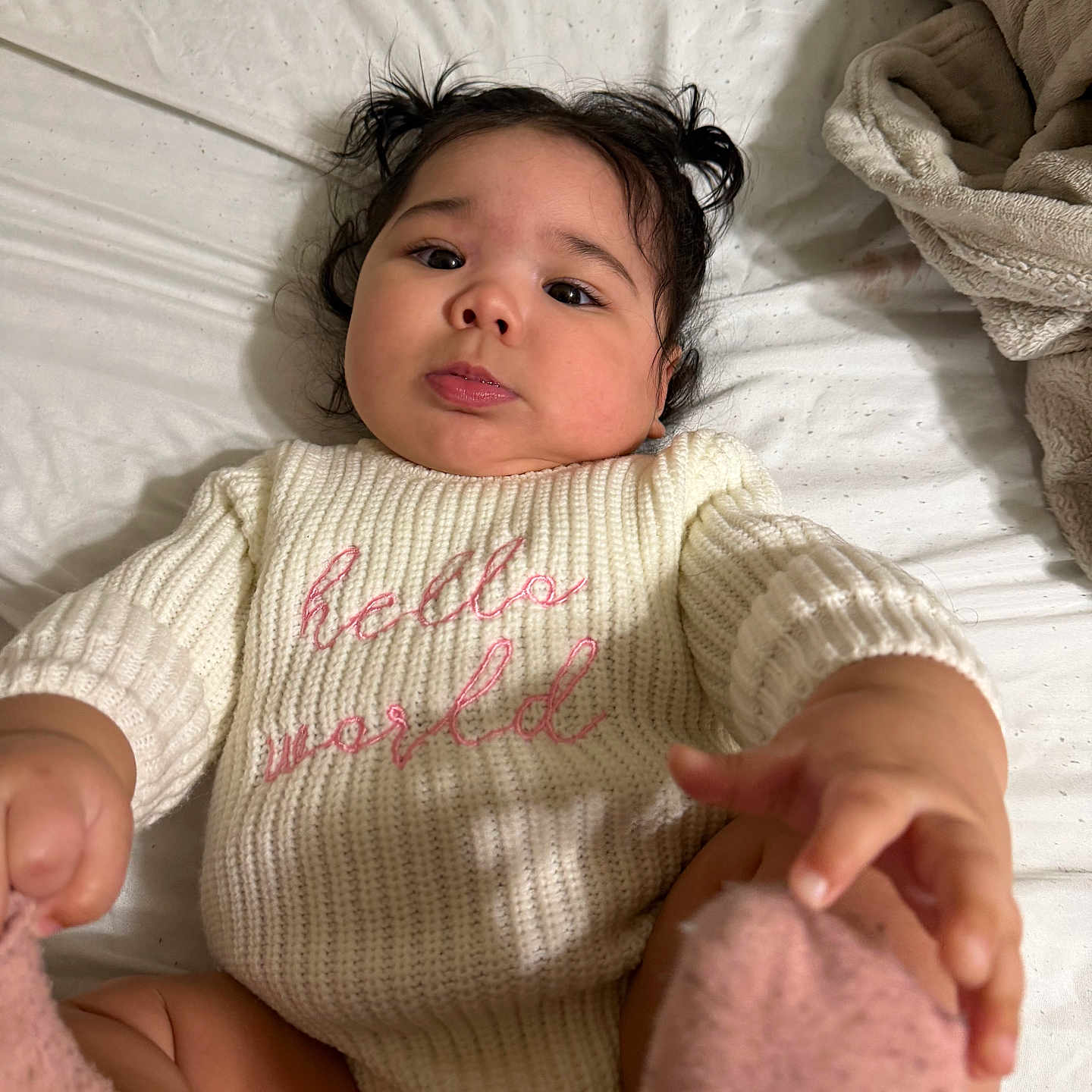 Sheraelys is registered to the contest to win money with this photo: baby, child, infant, pigtails, sweater, knitwear, bed, blanket, pink_socks, hand, face, cute, indoors, soft_texture, curious, lying_down, cozy, portrait, young_child, warm_clothing