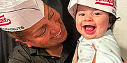 Angelina is registered to the contest to win money with this photo: adult, baby, black_shirt, celebration, curtain, cute, doughnut, face, fun, happy, hat, holding, indoor, joy, krispy_kreme, paper_hat, person, portrait, smiling, toddler