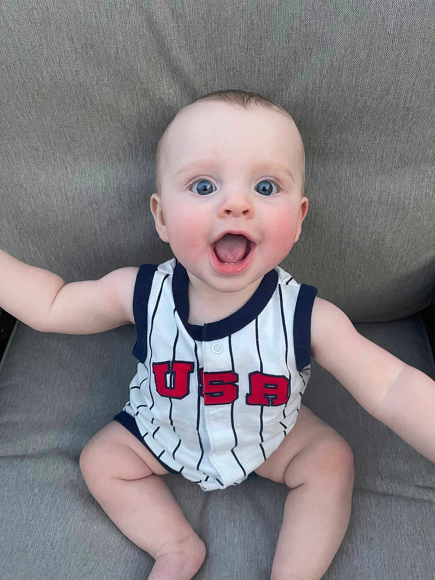 Brody joined the competition — help win amazing prizes! baby, child, smiling, happy, onesie, usa, blue_eyes, sitting, cute, infant, portrait, clothing, skin, face, expression, indoor, person, casual, seat, fabric
