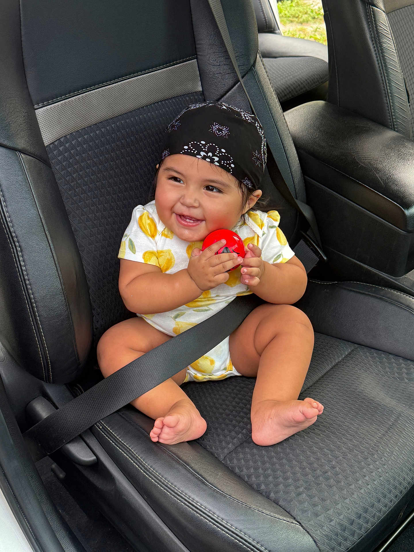 Megan is registered to the contest to win money with this photo: baby, child, smiling, bandana, red_ball, car_seat, seatbelt, black_leather, clothing, cute, happy, infant, indoors, person, sitting, toy, foot, hand, headwear, lemon_pattern
