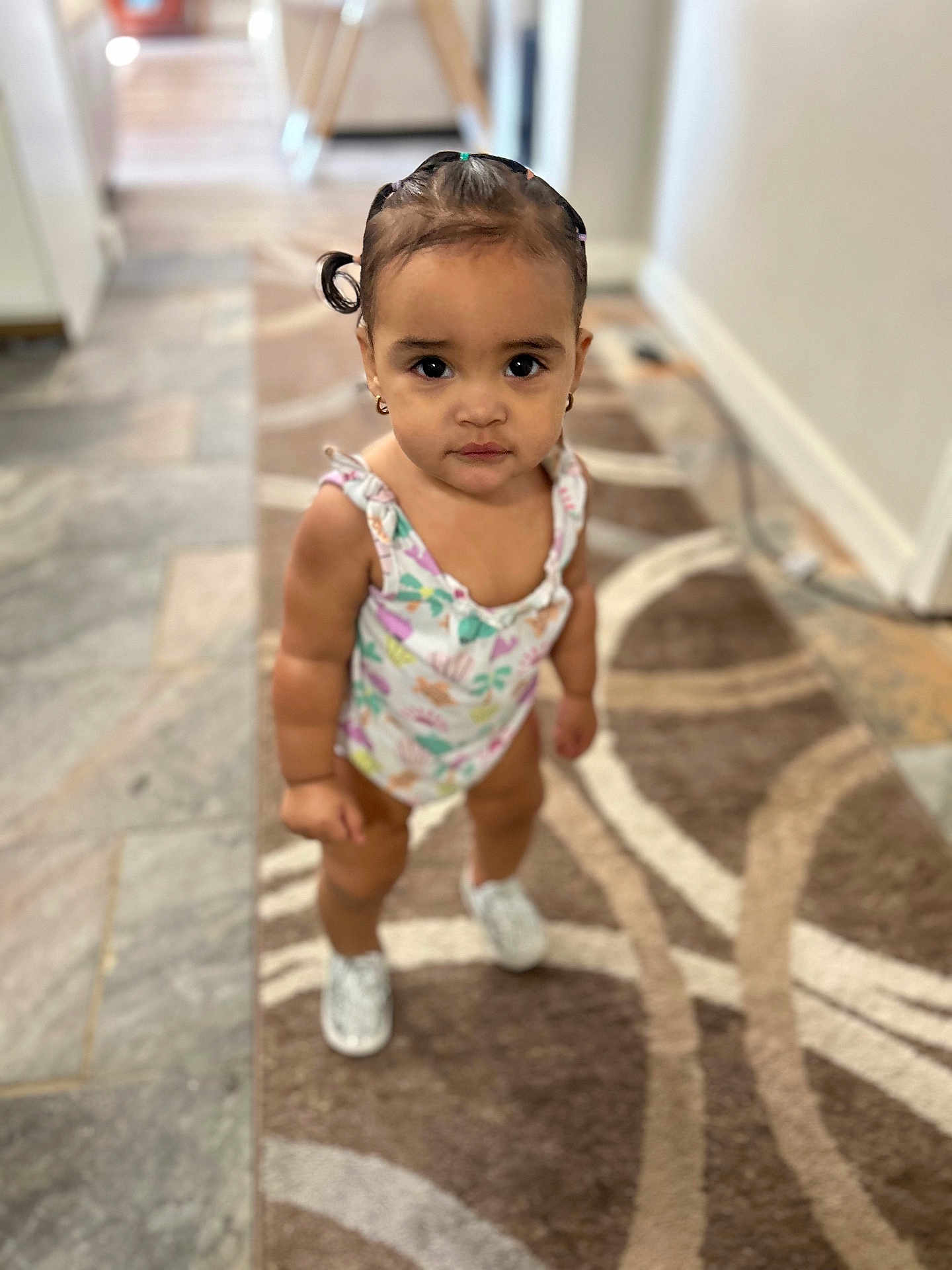 Daleyza joined the competition — help win amazing prizes! toddler, child, indoor, carpet, patterned_rug, standing, looking_at_camera, hair_tied, pigtails, onesie, footwear, flooring, home_interior, expression, cute, young_child, small_person, earrings, skin, person