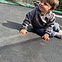 casual, child, curious, cute, daylight, grass, hoodie, jeans, netting, outdoor, playing, portrait, shadow, sitting, socks, sunlight, toddler, trampoline, trees, young