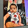 baby, child, bunny_ears, onesie, football_pattern, curly_hair, tablet_screen, adult, holding, indoor, temperature_display, time_display, date_display, puzzled_expression, cute, portrait, human, hand, clothing, face
