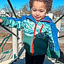 Kingston is registered to the contest to win money with this photo: child, curly_hair, smiling, jacket, playground, stairs, outdoor, daylight, blue_sky, houses, handrail, person, happy, casual_clothing, recreation, young, park, fun, kid, climbing