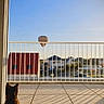 cat, balcony, railing, hot_air_balloon, sky, sunlight, shadow, building, house, window, car, outdoor, daytime, pet, animal, quiet, calm, urban, nature, view