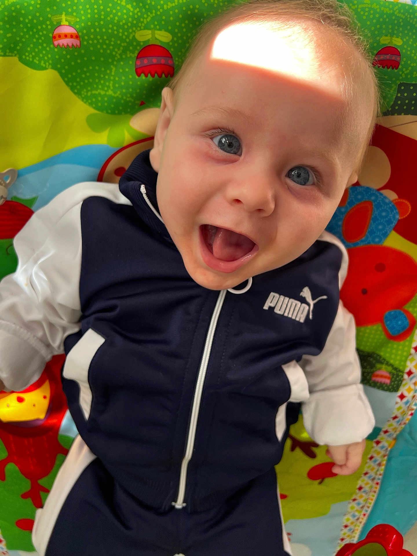 Milann participe au concours pour gagner de l'argent avec cette photo : baby, child, smiling, blue_eyes, jacket, puma, playmat, colorful, happy, infant, face, clothing, indoor, cute, young, person, joyful, expression, toy, patterned_background