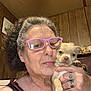 Ghost is registered to the contest to win money with this photo: brown_hair, casual_clothing, close_up, curly_hair, cute, dog, face, furniture, glasses, hand, home, indoor, person, pet, portrait, puppy, ring, small_dog, woman, wood_paneling