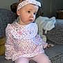 toddler, child, girl, headband, floral_pattern, long_sleeves, pink_clothing, leggings, sitting, couch, indoor, soft_lighting, portrait, cute, young_child, face, expression, home, blurry_background, cozy