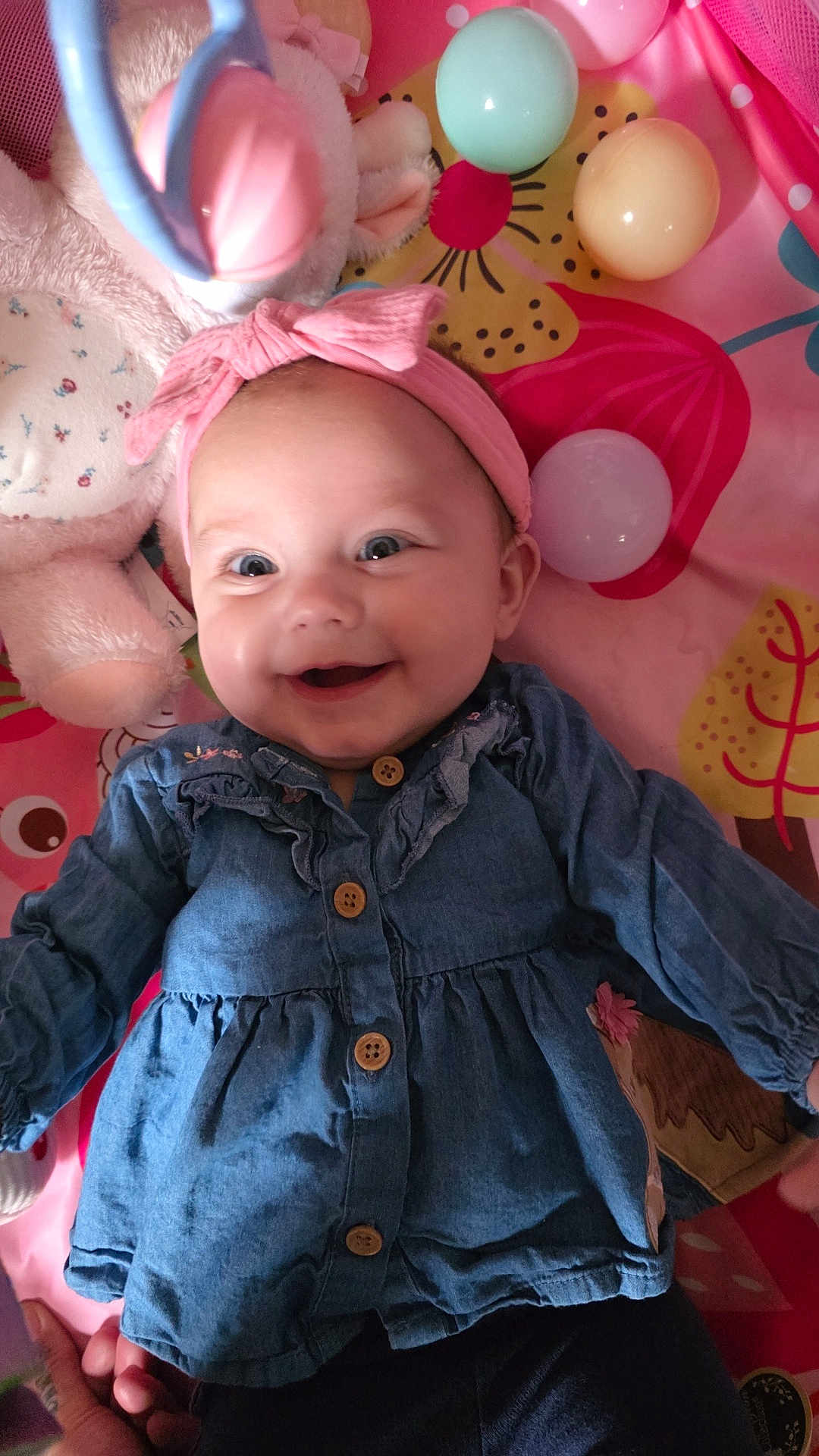 Faye joined the competition — help win amazing prizes! baby, infant, smile, headband, bow, denim_dress, toy, stuffed_animal, play_mat, plastic_ball, cheeks, eyes, portrait, cute, happy, lying_down, hands, clothing, indoor, colorful
