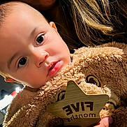 Zamir is registered to the contest to win money with this photo: baby, bear, blanket, child, close_up, cozy, cute, eyes, face, fur, hand, holding, indoor, infant, person, portrait, sign, soft_lighting, warm, wooden_star