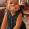 child, toddler, pacifier, video_call, smiling, indoor, living_room, couch, person, woman, adult, brick_wall, carpet, denim_clothing, long_hair, technology, screen, communication, happy, family